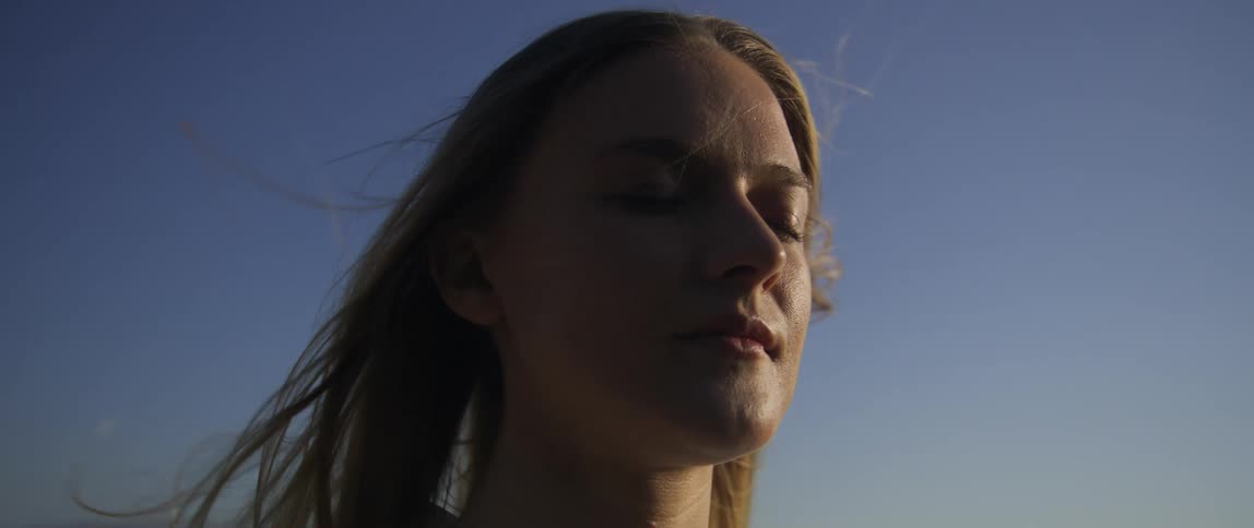 A woman slowly opens her eyes as the wind blows her hair