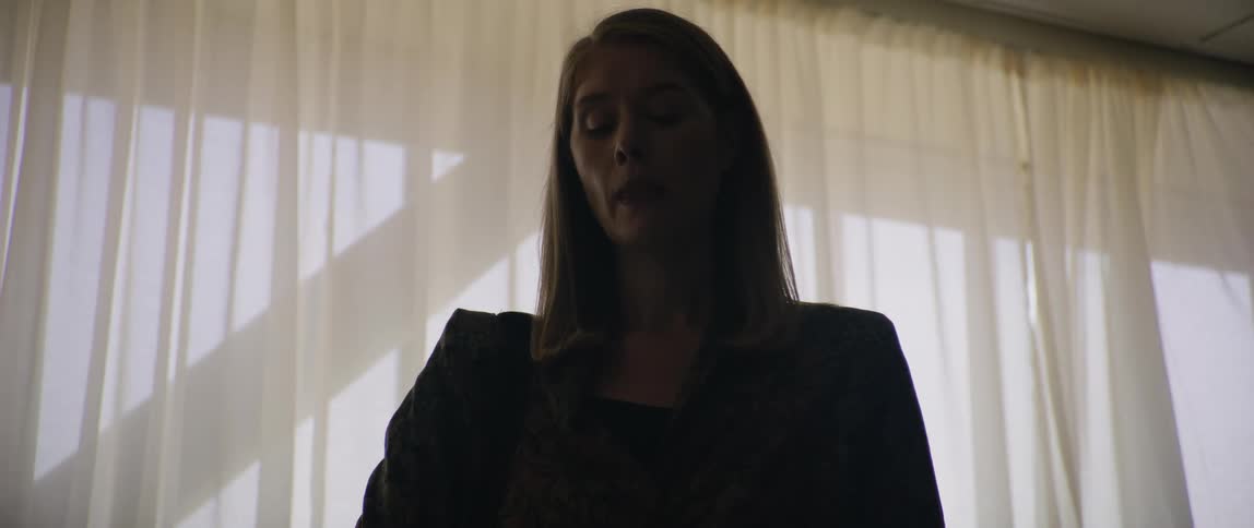 Woman in black blazer in a room with a window in the background with curtain