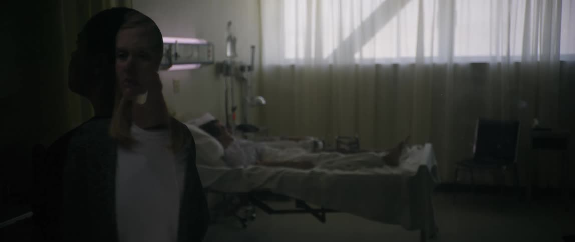 Reflection of a woman looking at a clinical room and a person sleeping in the hospital