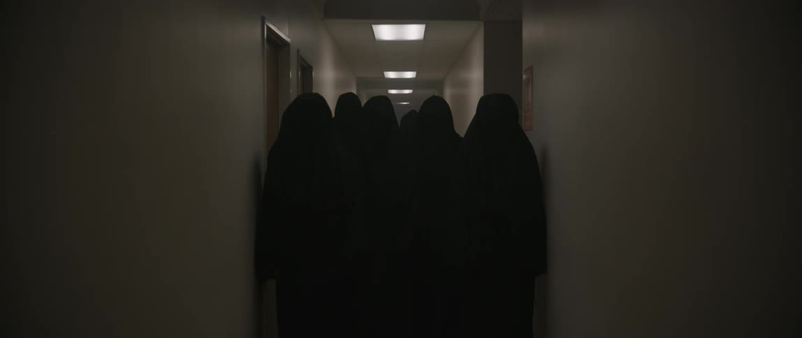 A group of people in dark robes stand in a lobby as the lights go off leaving the atmosphere pitch black