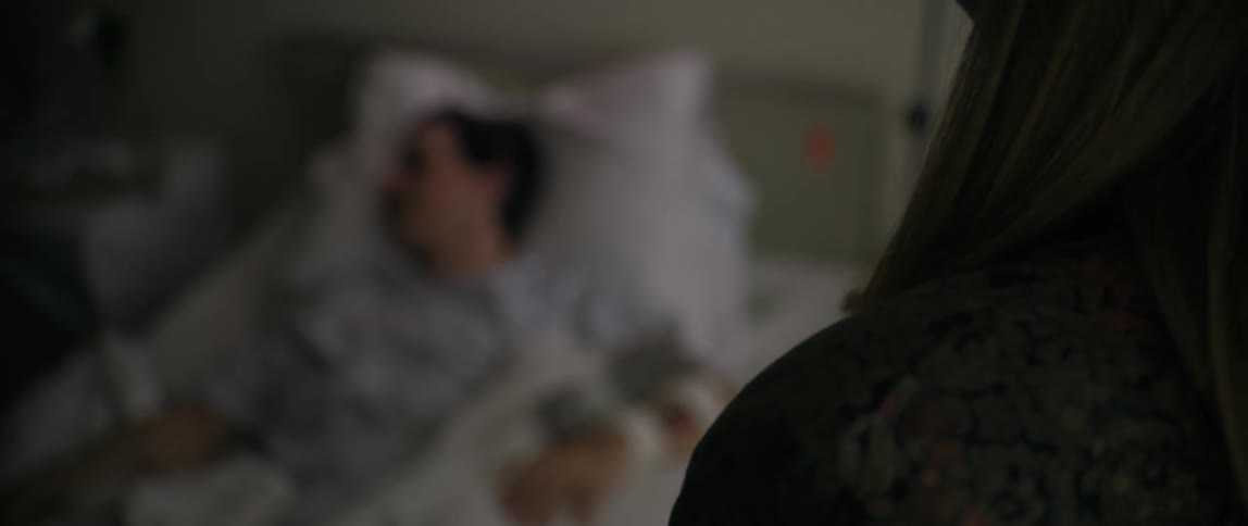 Woman talking excitedly and in the background a patient lying in a hospital bed