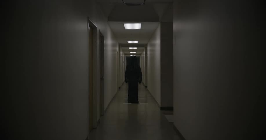 A frightening person standing in a hotel hallway wearing dark clothing