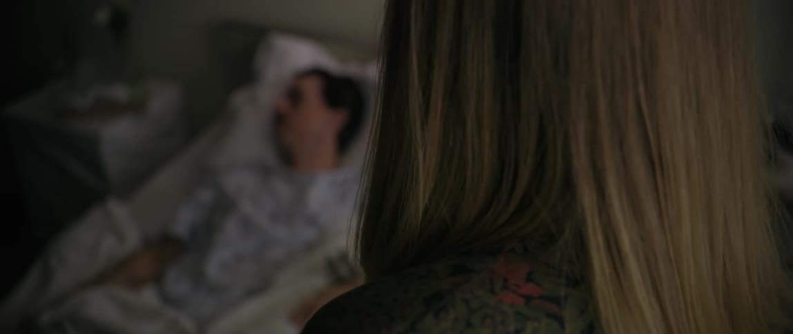 A woman speaks while a man lays in a hospital bed