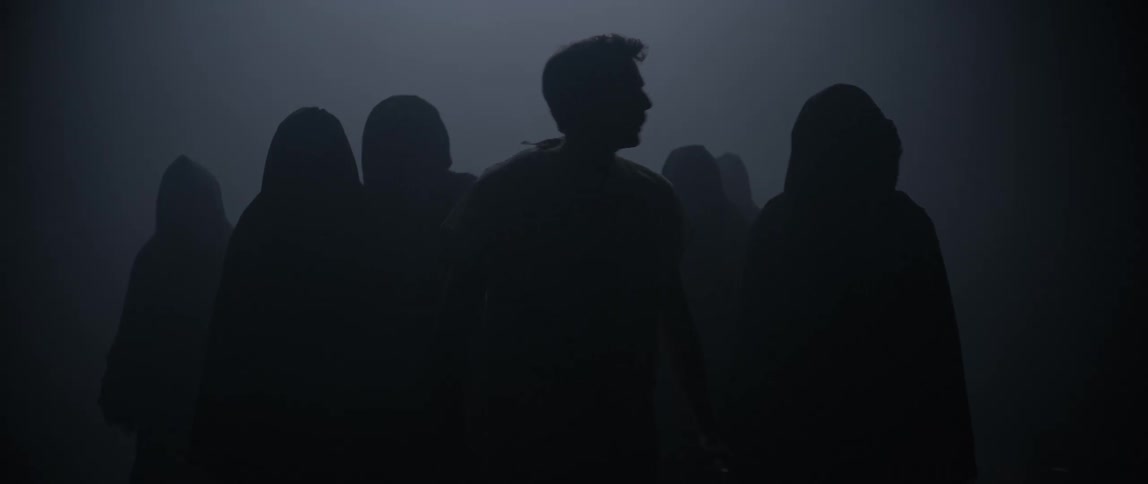 A small crowd of people wearing dark clothes walk towards the camera