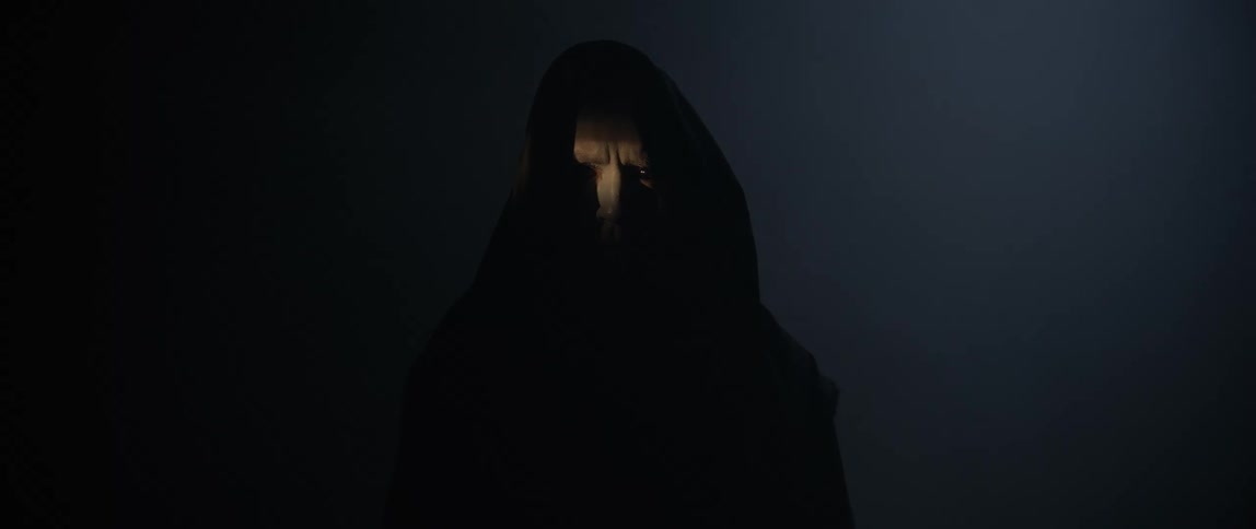 Man in black hood with red and black eyes staring