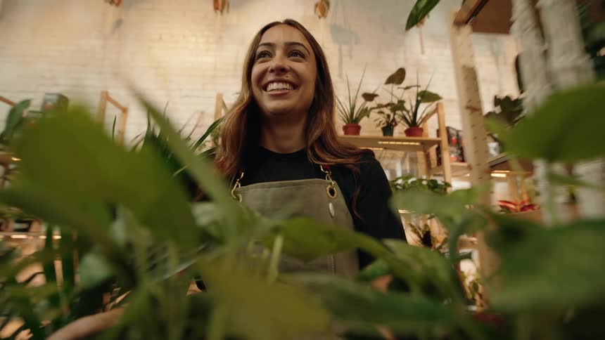 A woman smiles and laughs as she pushes a trolley with plants around a room
