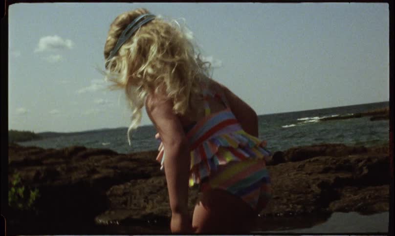A young girl points to a pool of water on an ocean coast on a summer day