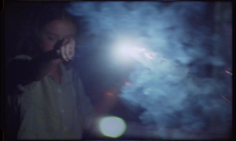 A barefoot women lights a small fire or sparkler on the ground at night and waves it around creating smoke