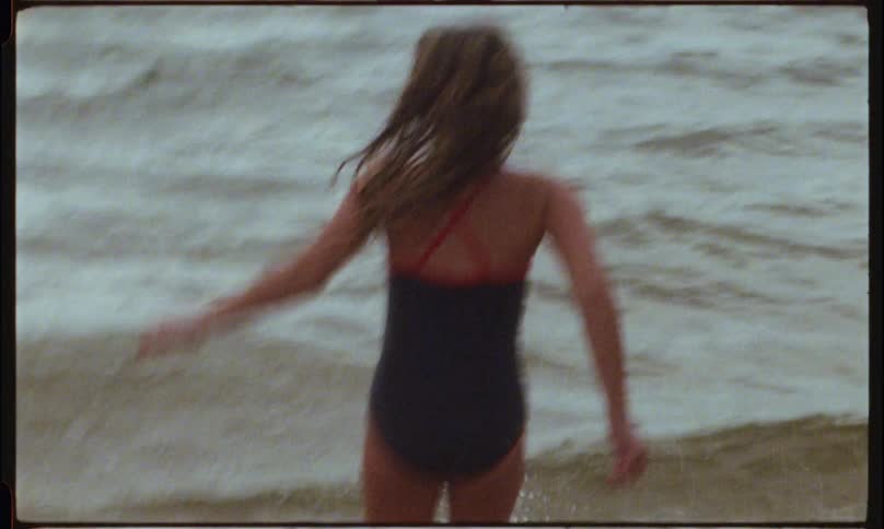 A girl walks into the beach water at sunset