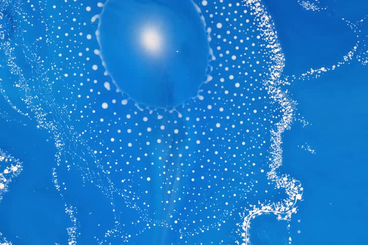 A striking close up of white particles swirling in vibrant blue liquid creating circular organic patterns around a glowing center