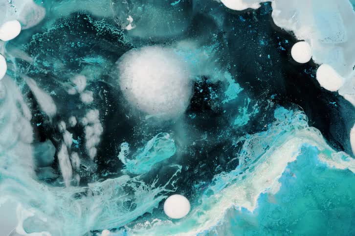 A highly magnified view of abstract blue and white liquids swirling with suspended spheres creating a cosmic or underwater effect