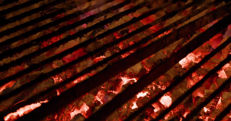 Flames rise from hot charcoal on a grill glowing in the darkness