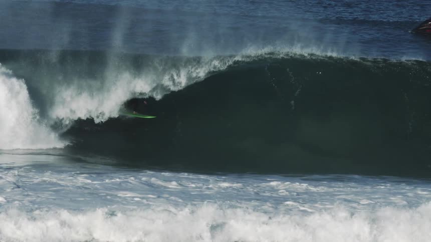 Surfer riding barrel of a huge wave on a green surfboard