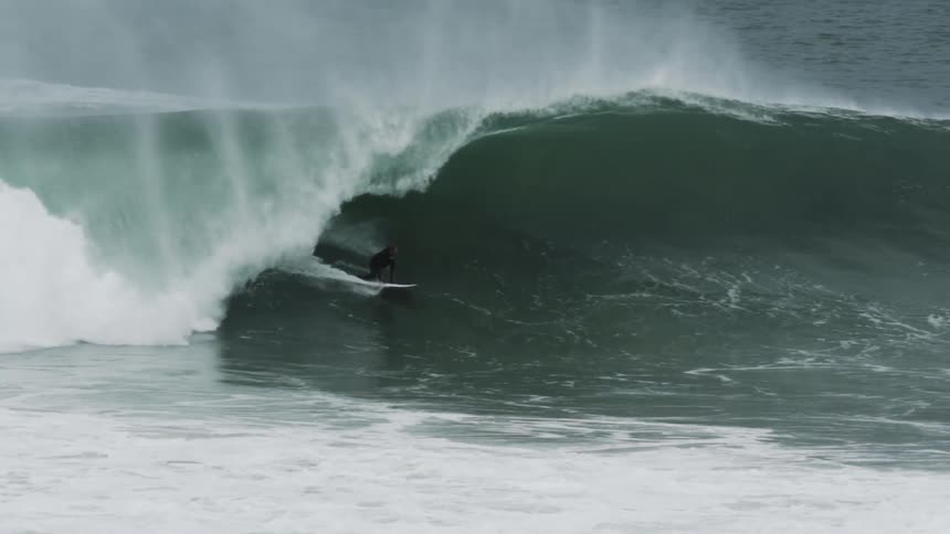 A surfer rides inside a massive barreling wave at the beach showcasing skill and timing