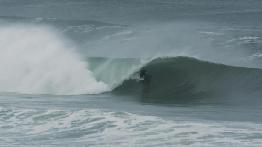 Surfer rides a huge waves and stays on his surfboard as it curls overhead and covers him with water