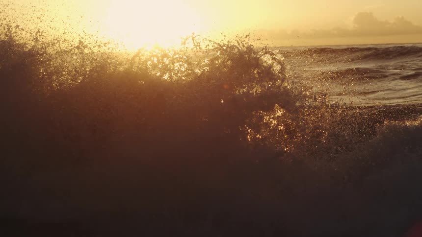 Waves splash into the air as they roll in to shore and the sun shines brightly on the horizon