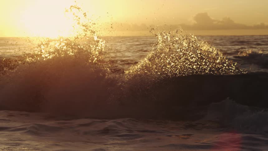 An ocean wave is breaking on its surface on a day with the bright sun strongly behind it
