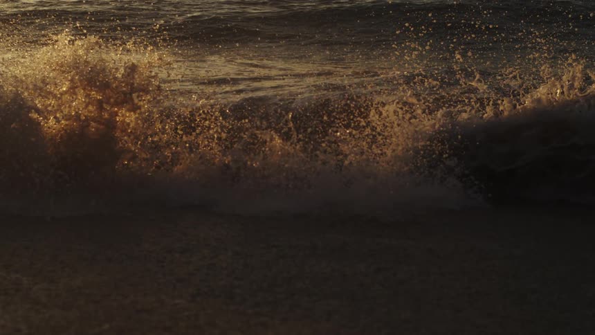 A small wave crashes on the sand