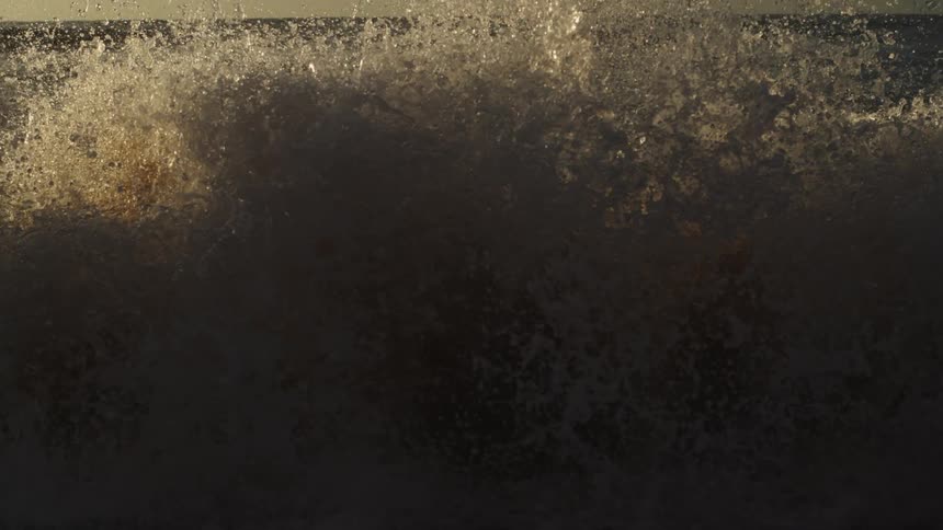 Water droplets sparkle and waves splash as they roll in to shore