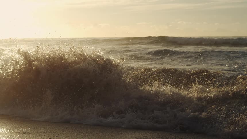 Huge waves approach and crash against the seashore at dusk