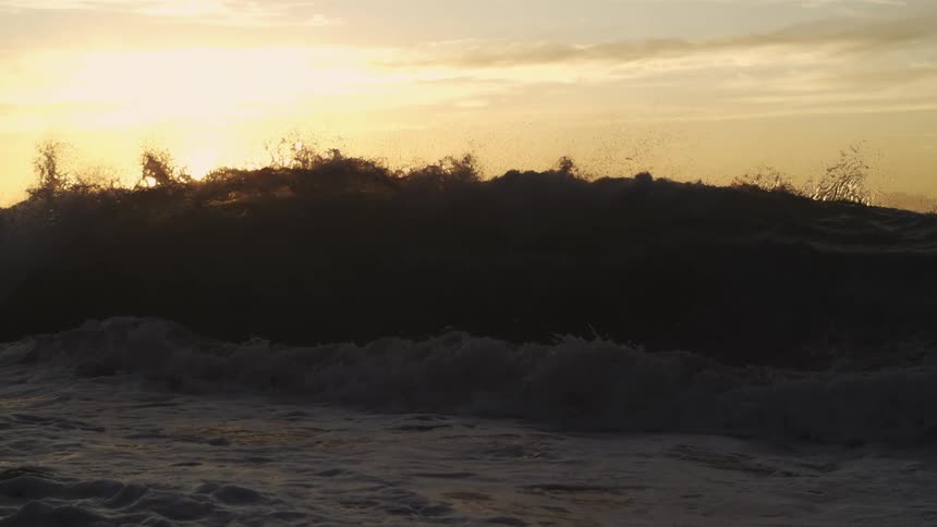 Wave splashing as it rolls in under a sunset sky