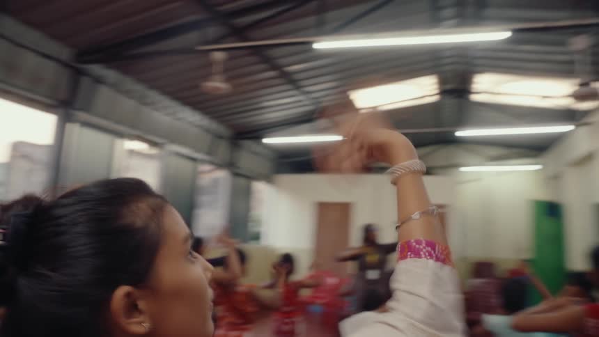 A group of children and teenagers practise dance moves with an instructor in a hall