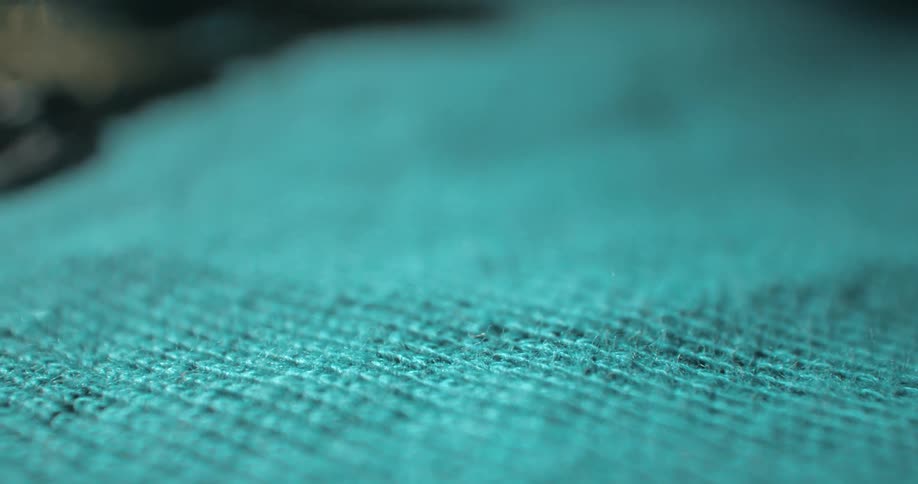 An extreme closeup of teal woven fabric showcases detailed texture and pattern in soft focus