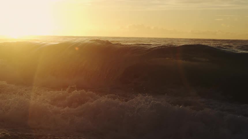 The sun is rising on the large waves by the beach