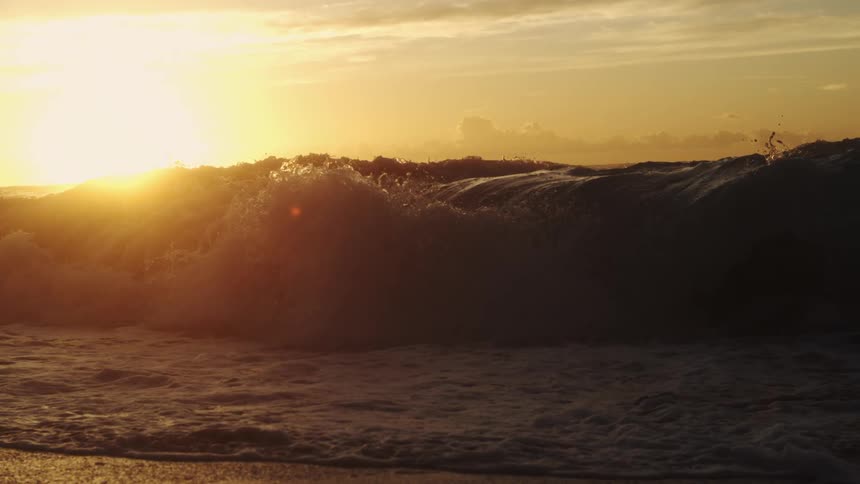 Waves splash and roll in to shore as the sun shines brightly on the horizon