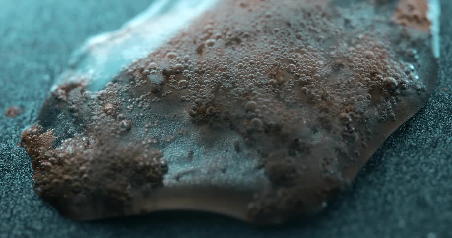 Reddish brown bubbles clinging to the surface of an object lying underwater on a flat surface shift