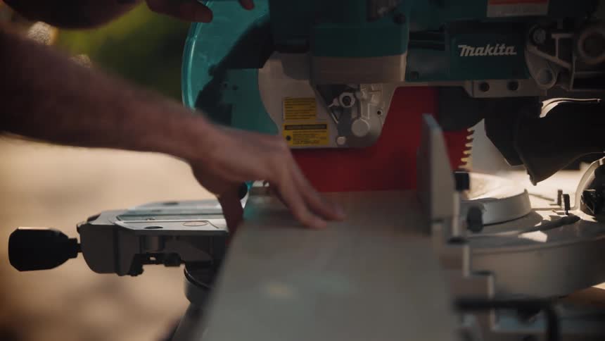A closeup shows a persons hand carefully guiding a piece of wood through a circular saw in a woodworking or construction setting