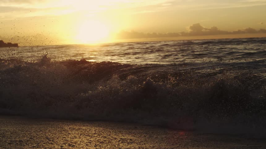 Wave breaking on the beach sand and the sunrise on the horizon