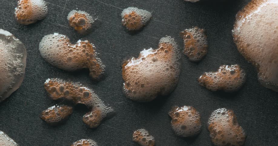 Extreme closeup of a brown liquid bubbling and foaming on a surface