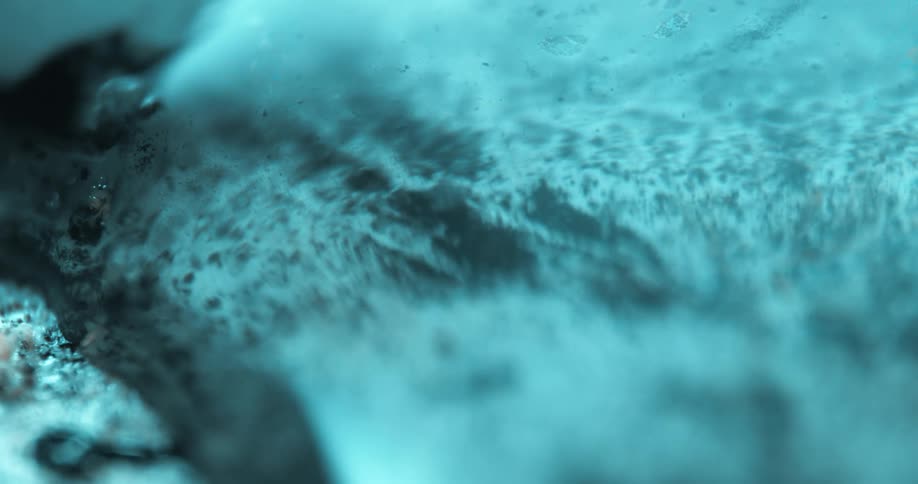 A slimy blue liquid slowly flows across a surface in a microscopic view
