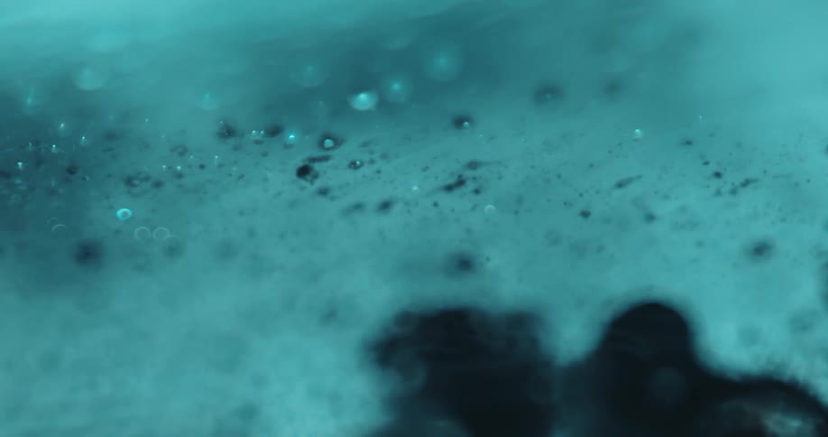 Pale blue substance flows slowly while bubbles on its surface pop