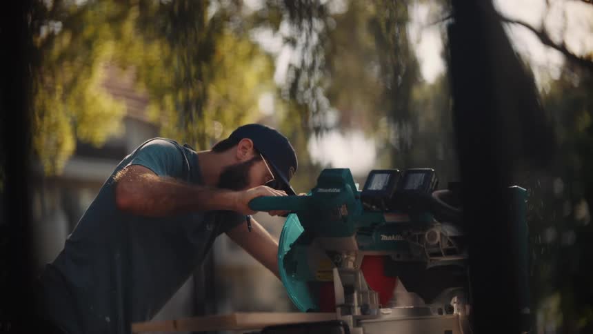Male carpenter uses a table saw while working outdoors