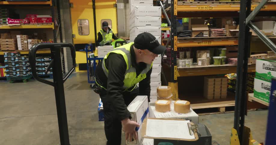 Warehouse workers are actively moving and stacking boxes in an organized industrial storage facility