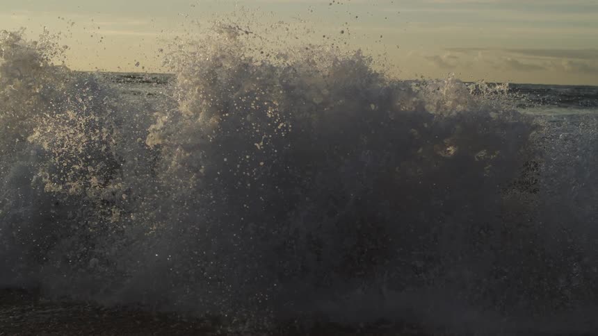 Wave approaches and splashes against the shore at dusk