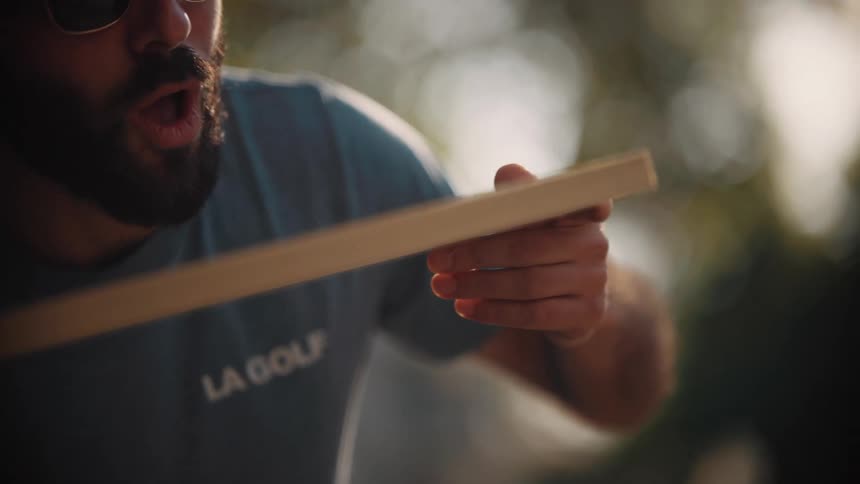 Close up of a man holding and blowing dust off the surface of a piece of wood