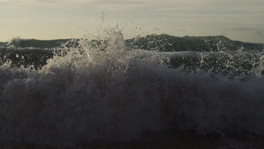 Ocean wave approaches and splashes against the shore at dusk