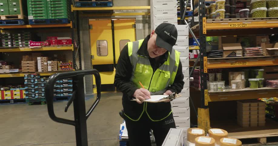 A food warehouse employee writes on a clipboard