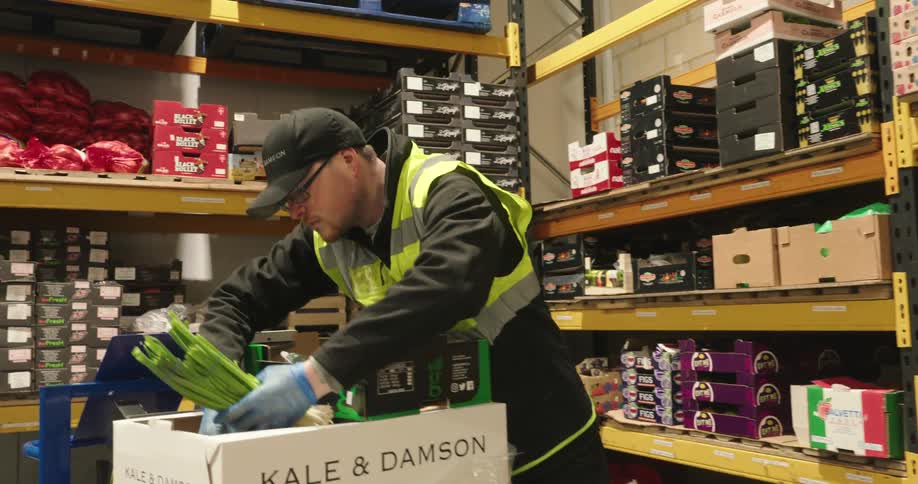 Warehouse employee scanning then packing produce in cardboard box