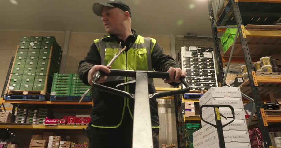 The worker is pulling a pallet jack in the warehouse