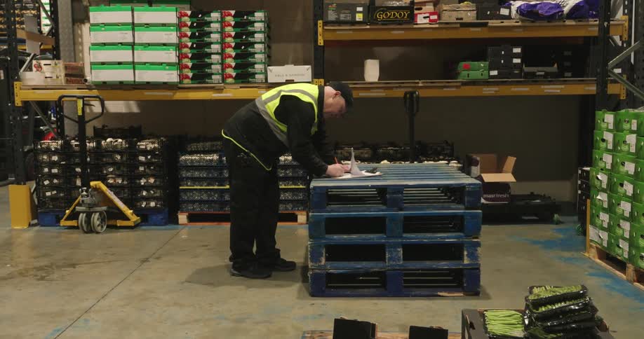 A man is writing on his clipboard on a pallet