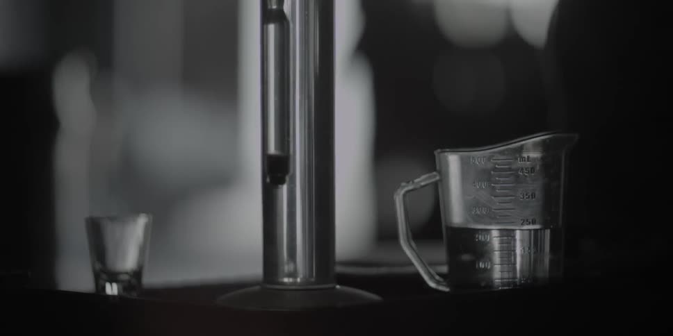 A clear cylinder descends into a beaker of liquid on a table