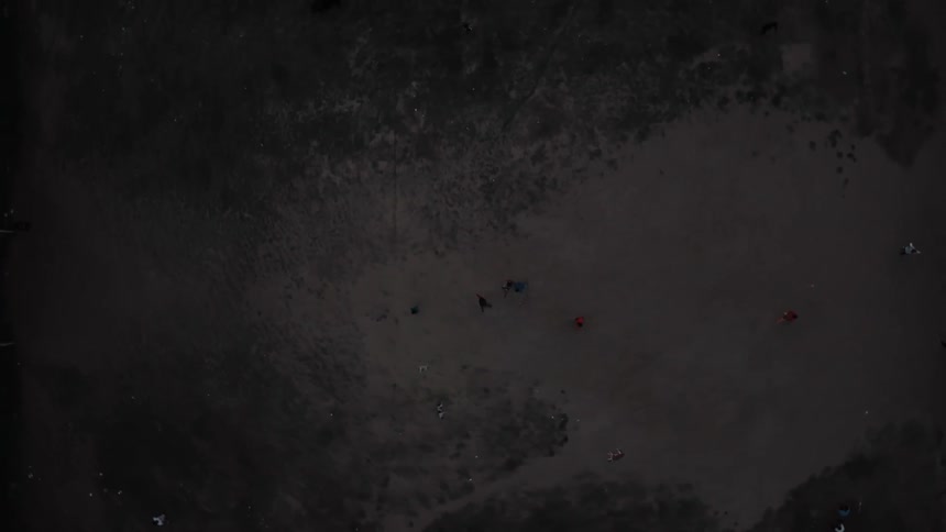 Dirt field with players spread out is seen from above in low lighting