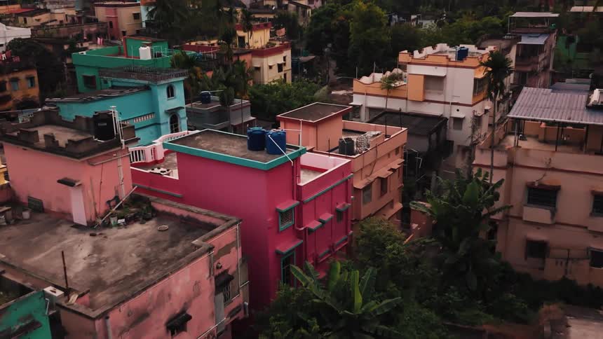 A series of closely built residential buildings in various colors stand together in a city with some surrounded by trees all seen in daylight