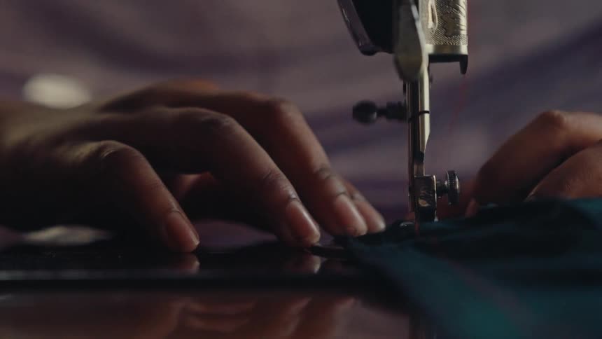 A womans hands passing a piece of cloth through the needle of a sewing machine in slow motion
