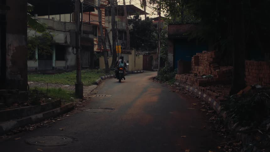 A man riding a motorcycle with a woman seated behind him drives down an empty street at sunrise