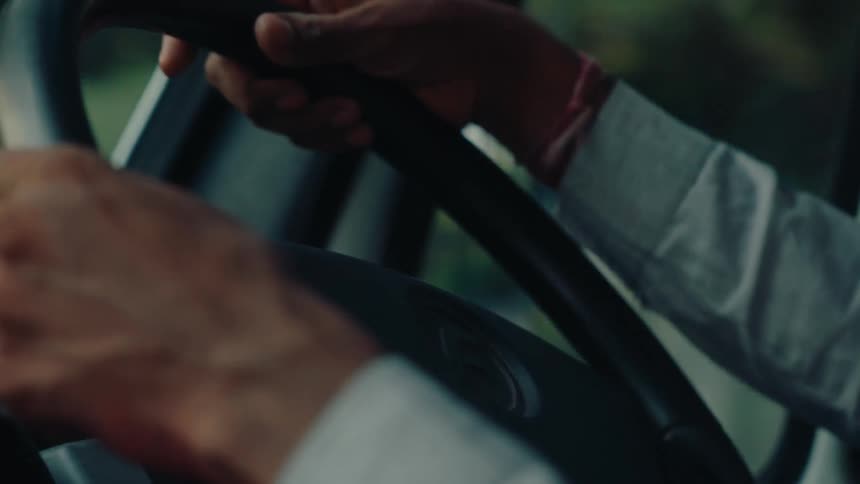 Pair of hands of a person handling a steering wheel of a moving vehicle